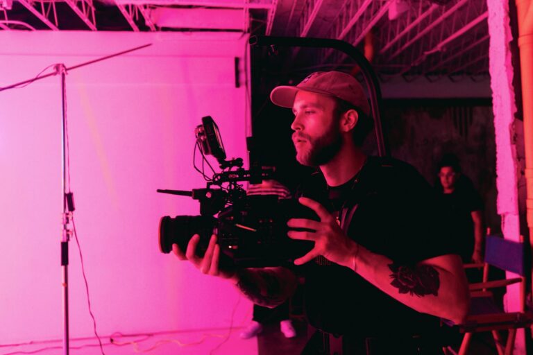 A filmmaker captures a scene using a professional camera in a studio with pink lighting.