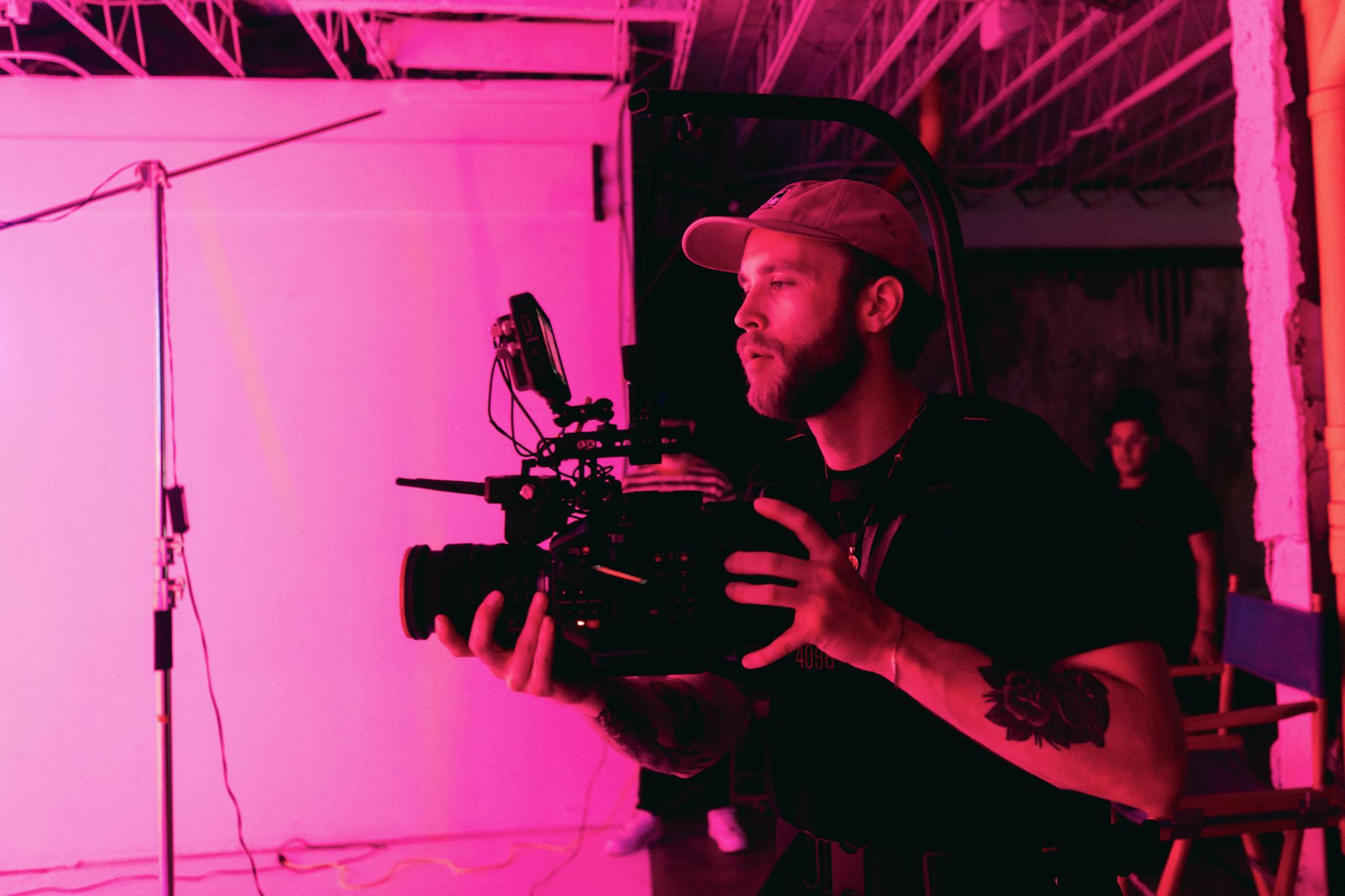 A filmmaker captures a scene using a professional camera in a studio with pink lighting.